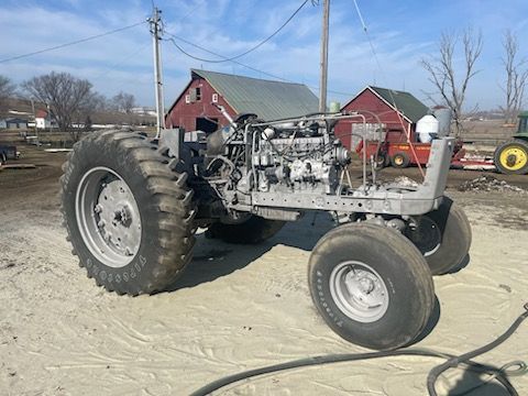an old tractor is parked in a dirt field in front of a barn