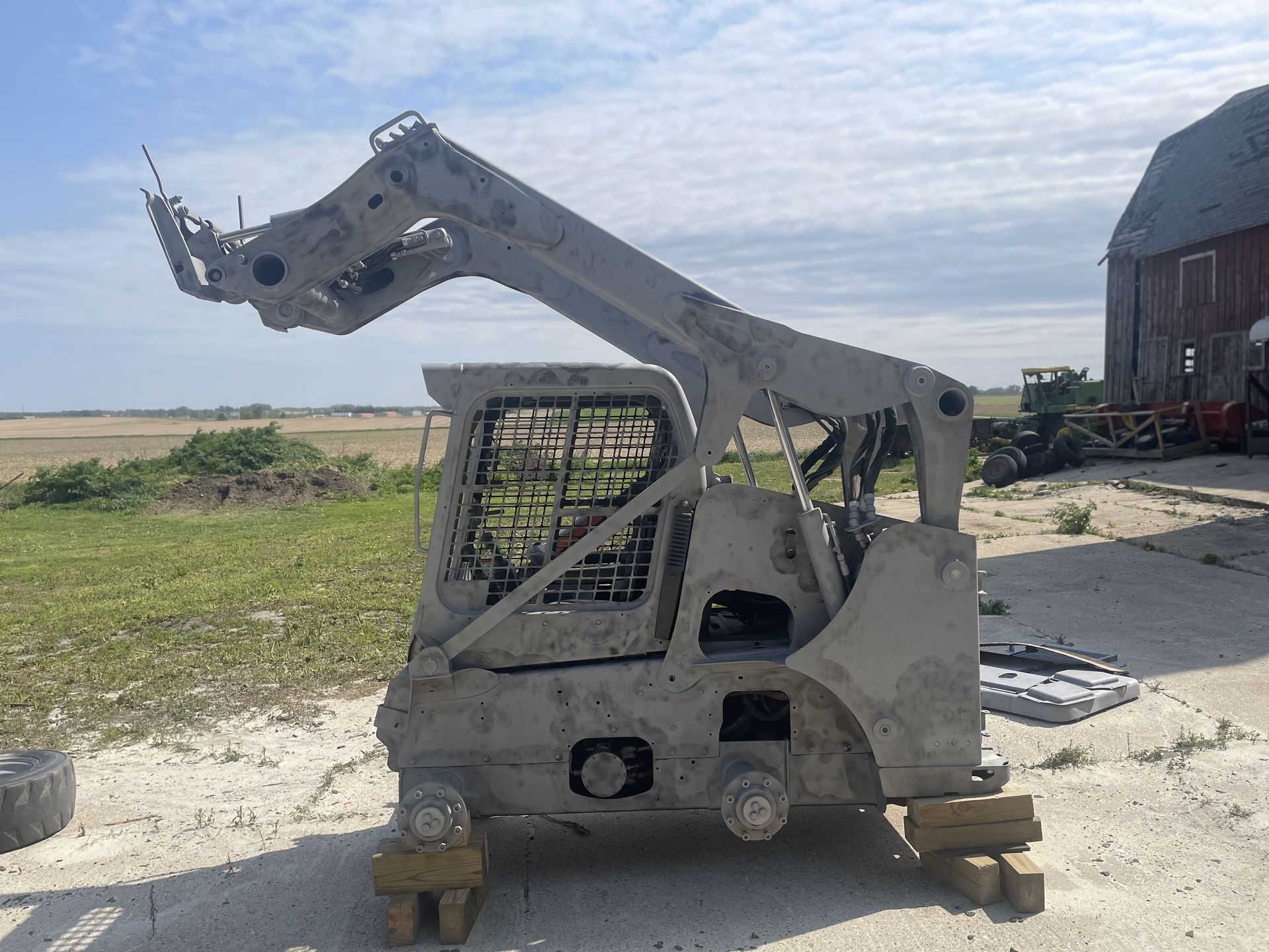 A piece of machinery is sitting in the dirt in front of a barn.