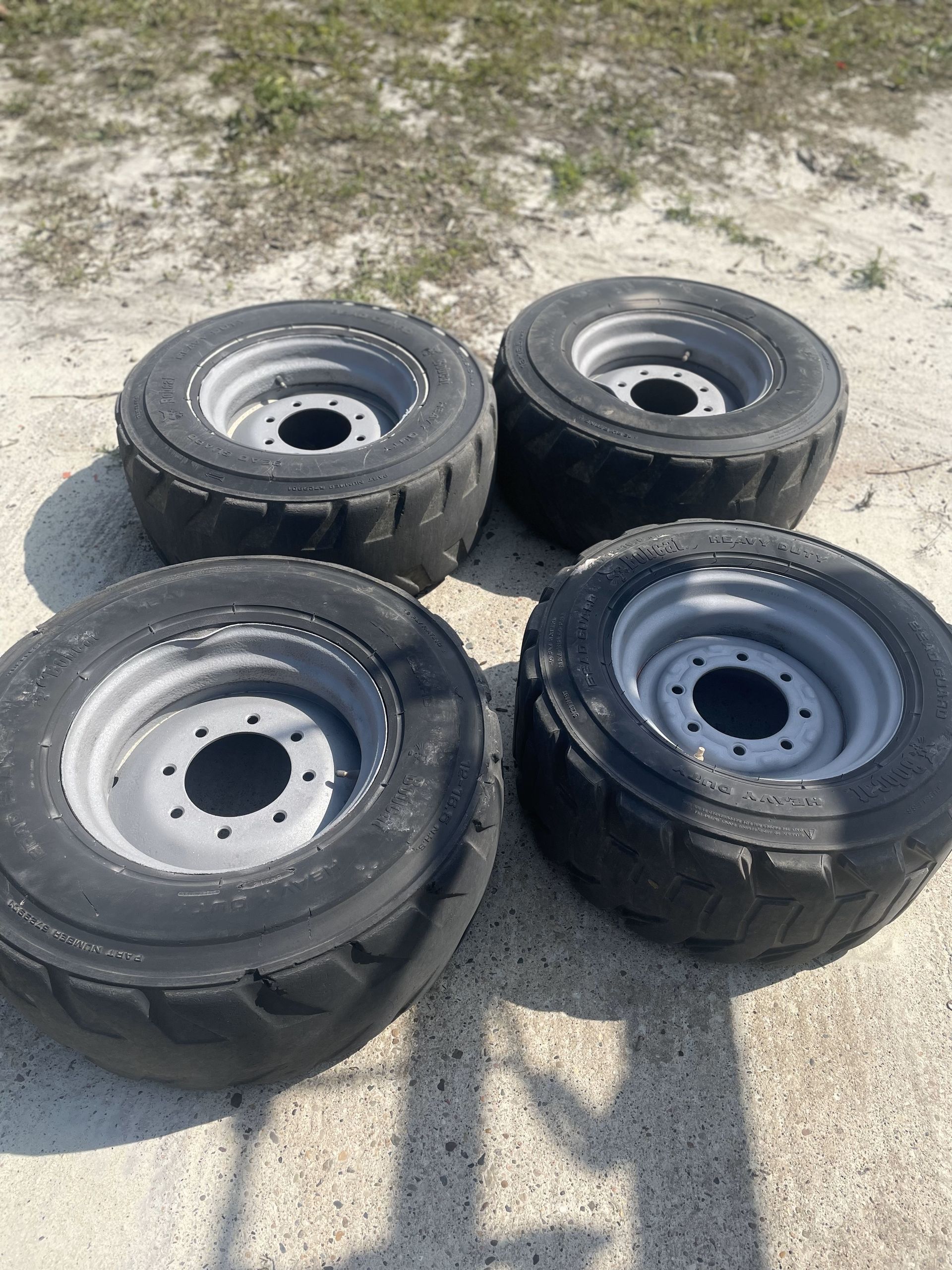 Four tires and rims are sitting on a sandy surface.