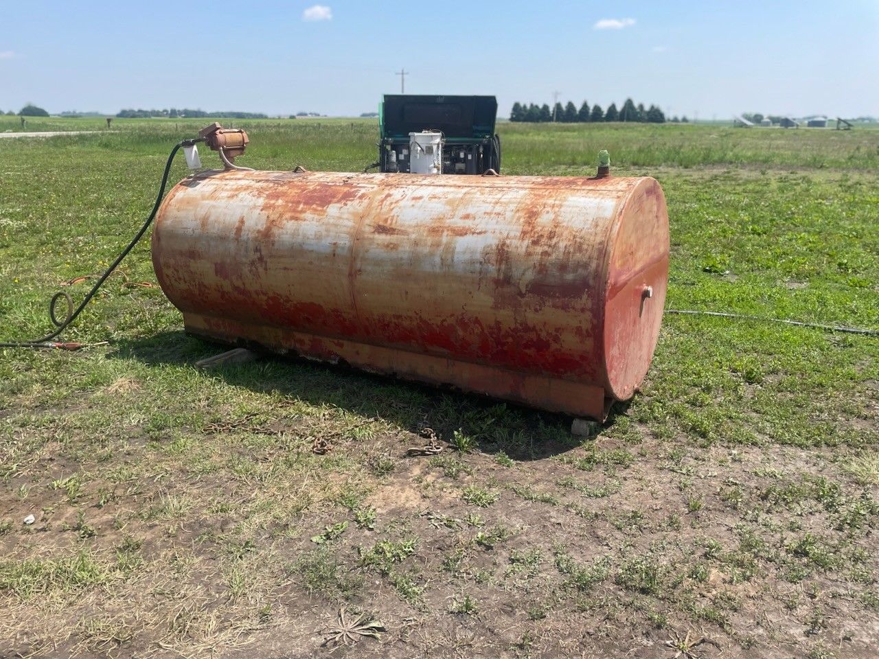 A large rusty tank is sitting in the middle of a grassy field.