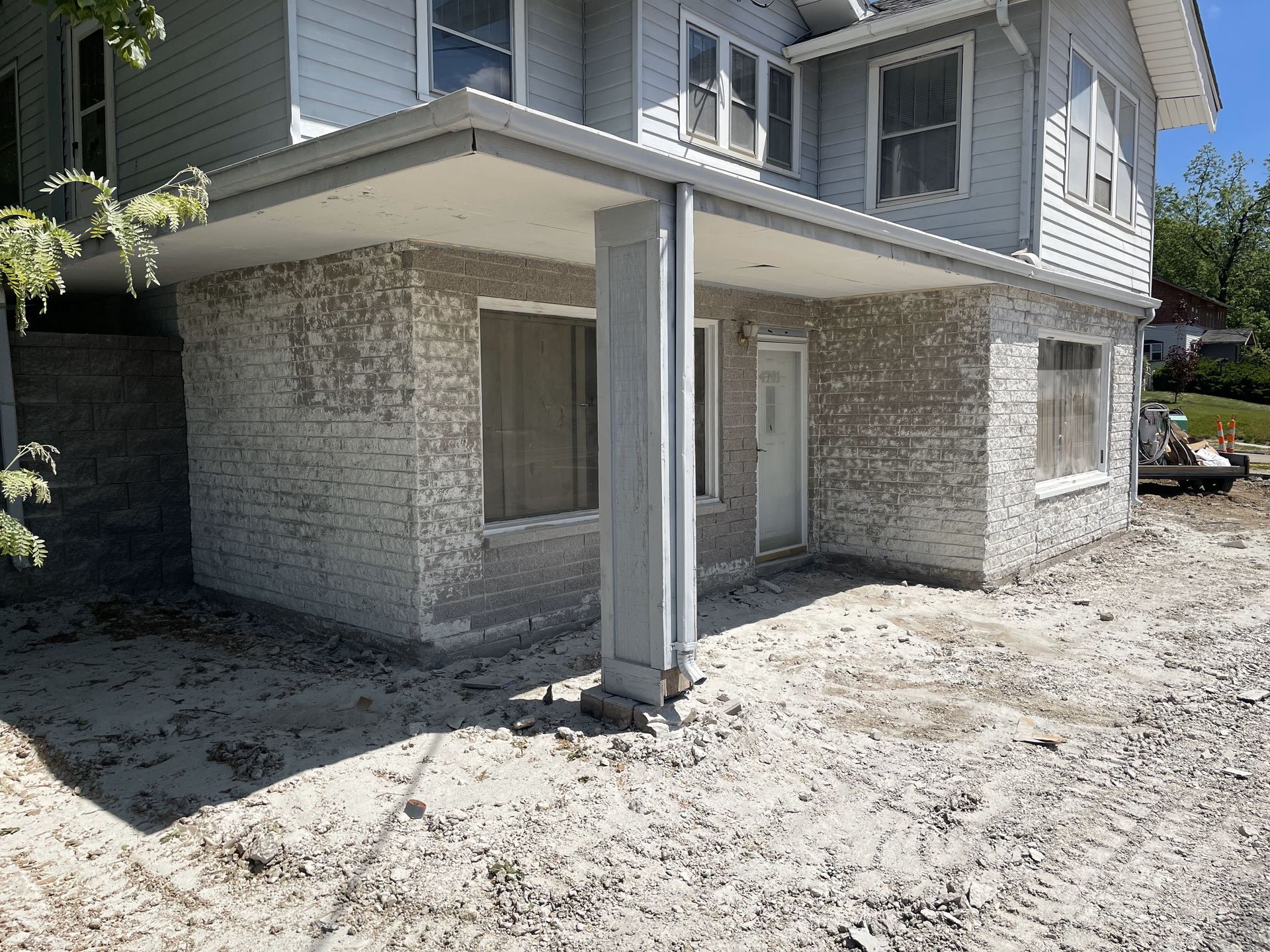 Exterior of a two-story house with a covered entranceway. Walls are stucco-covered brick; the ground is dirt.