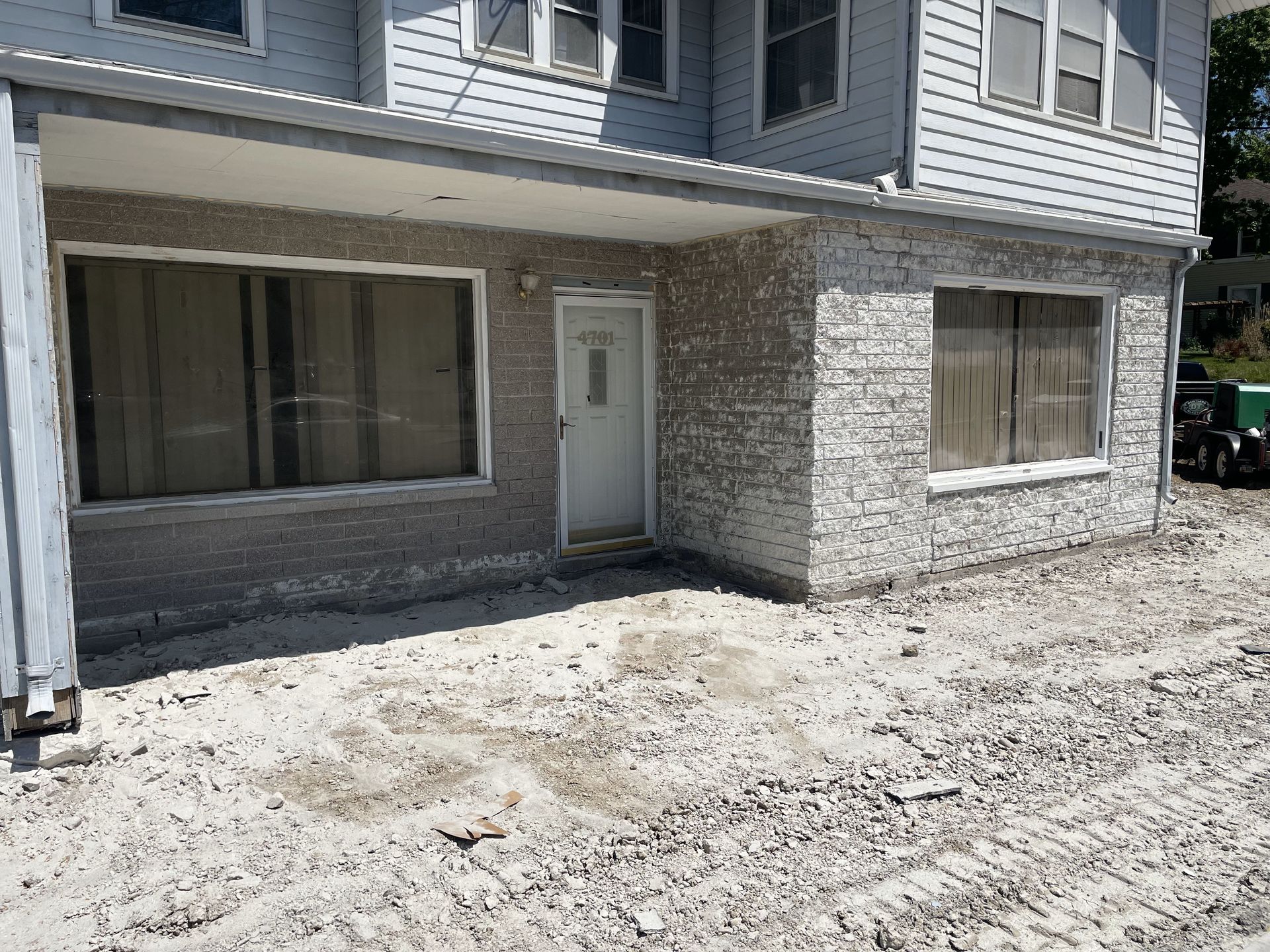 A two-story building with a ground-level entrance. The exterior features a textured brick design and dirt/gravel ground cover.