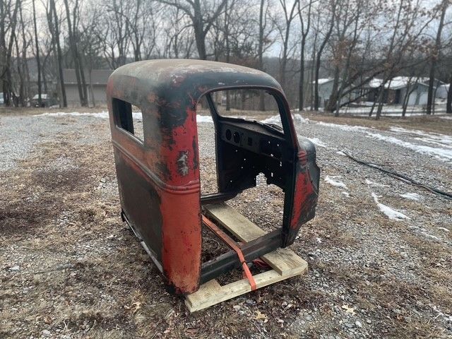 An old truck cab is sitting on a wooden pallet in a field.