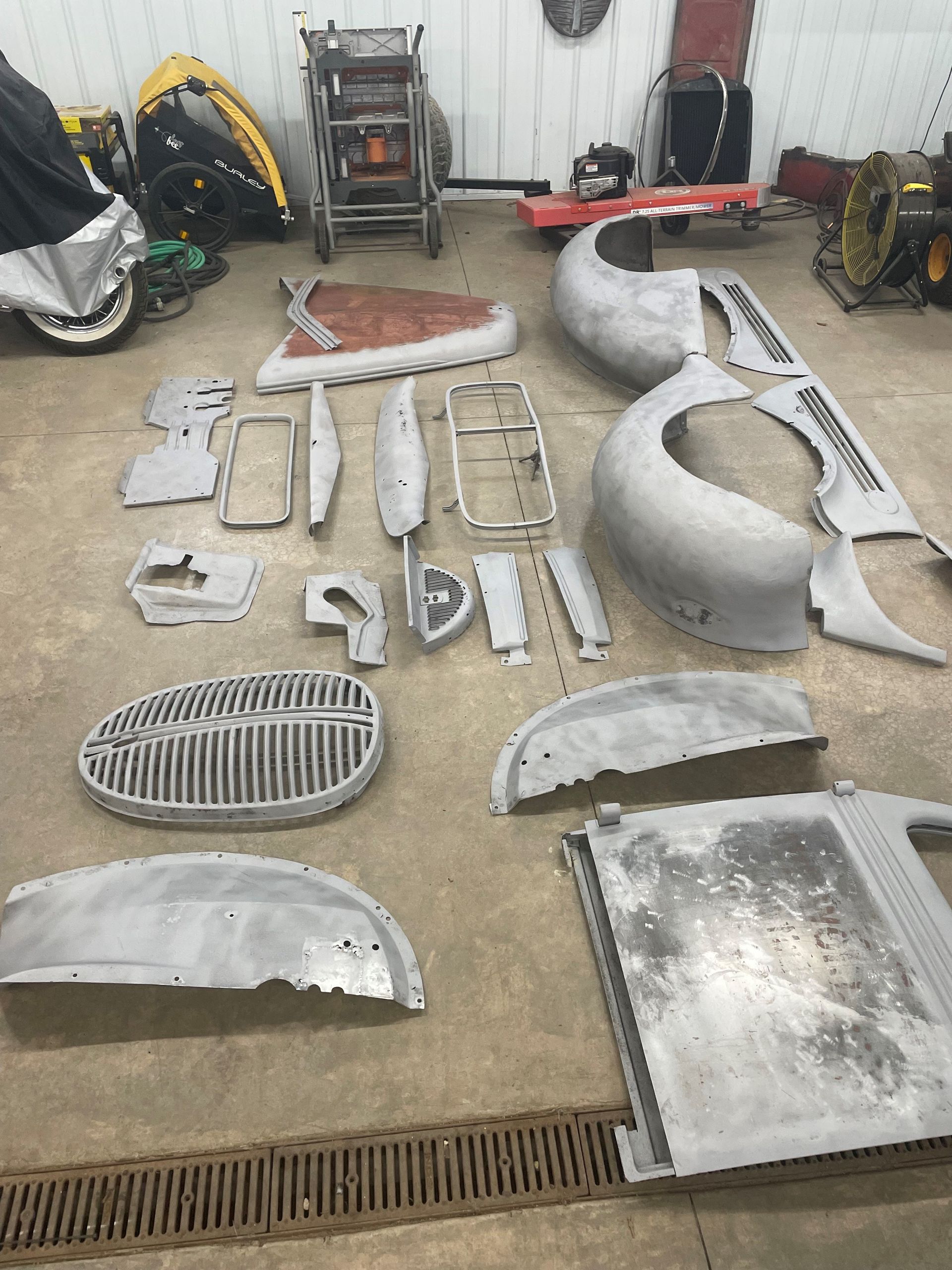 A bunch of car parts are laying on the ground in a garage.