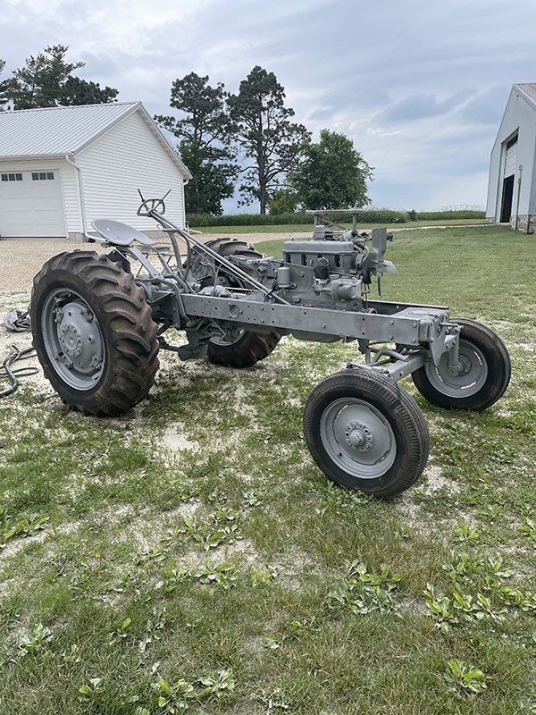 an old tractor is sitting in the grass in front of a garage