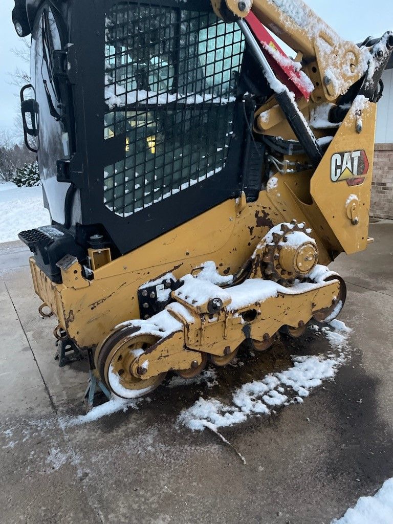 A cat skid steer is parked on the side of the road in the snow