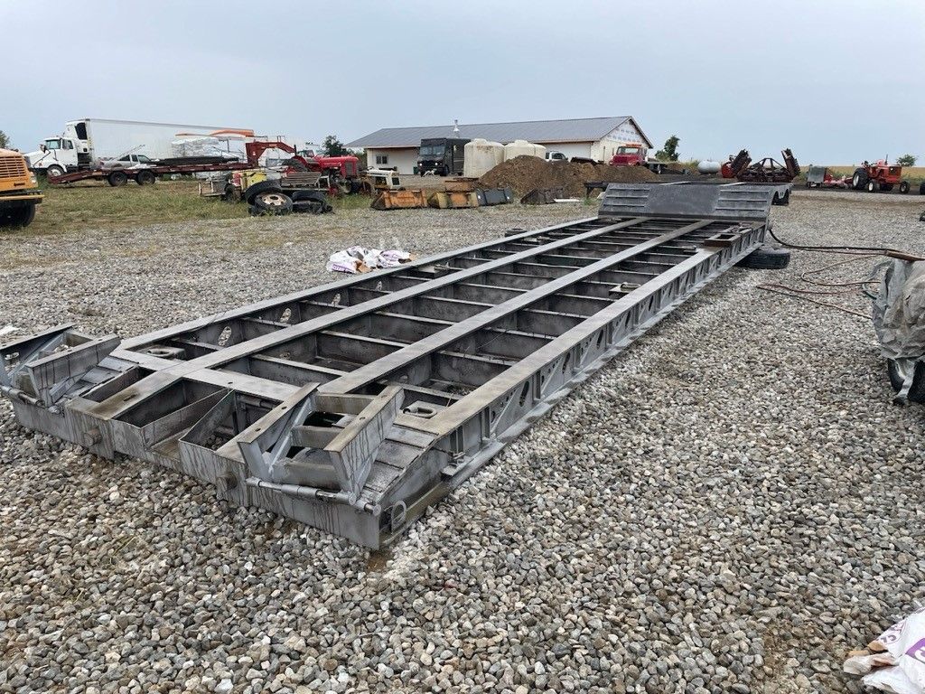 a trailer is parked in a dirt lot next to a pile of pipes