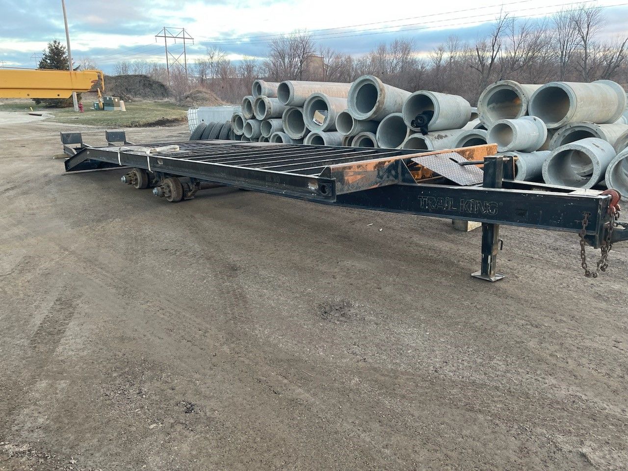 a trailer is parked in a dirt lot next to a pile of pipes