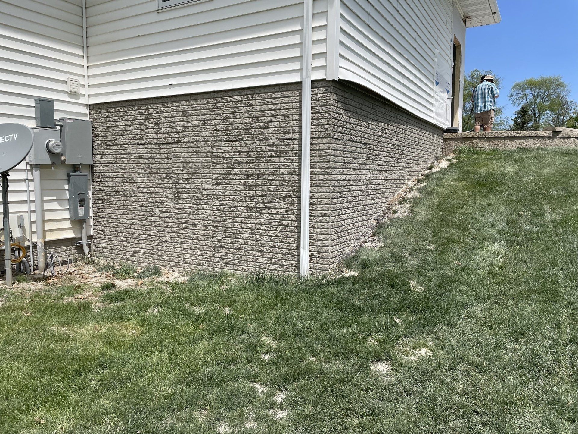 a house with a brick foundation is sitting on top of a lush green hillside