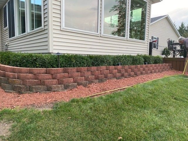 a man is working on a retaining wall in front of a house