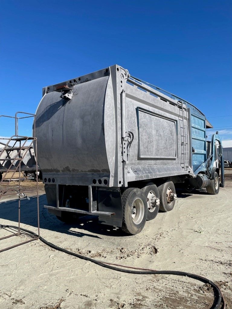 a garbage truck is parked in a dirt lot