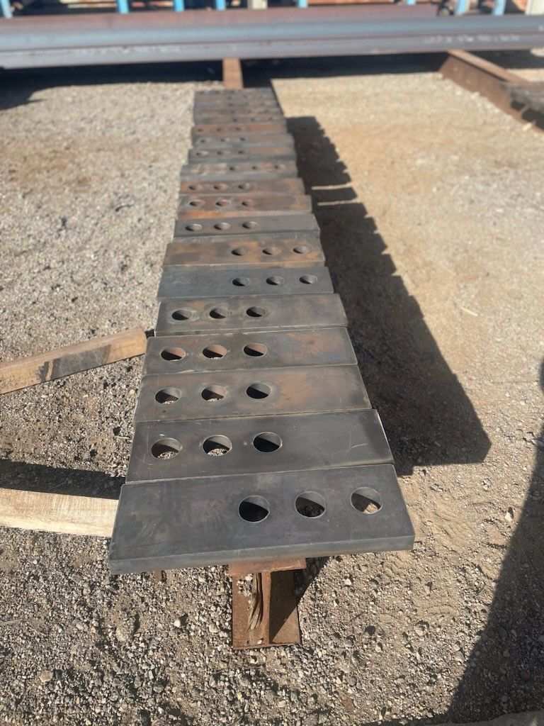 a row of steel plates with holes in them are sitting on top of gravel
