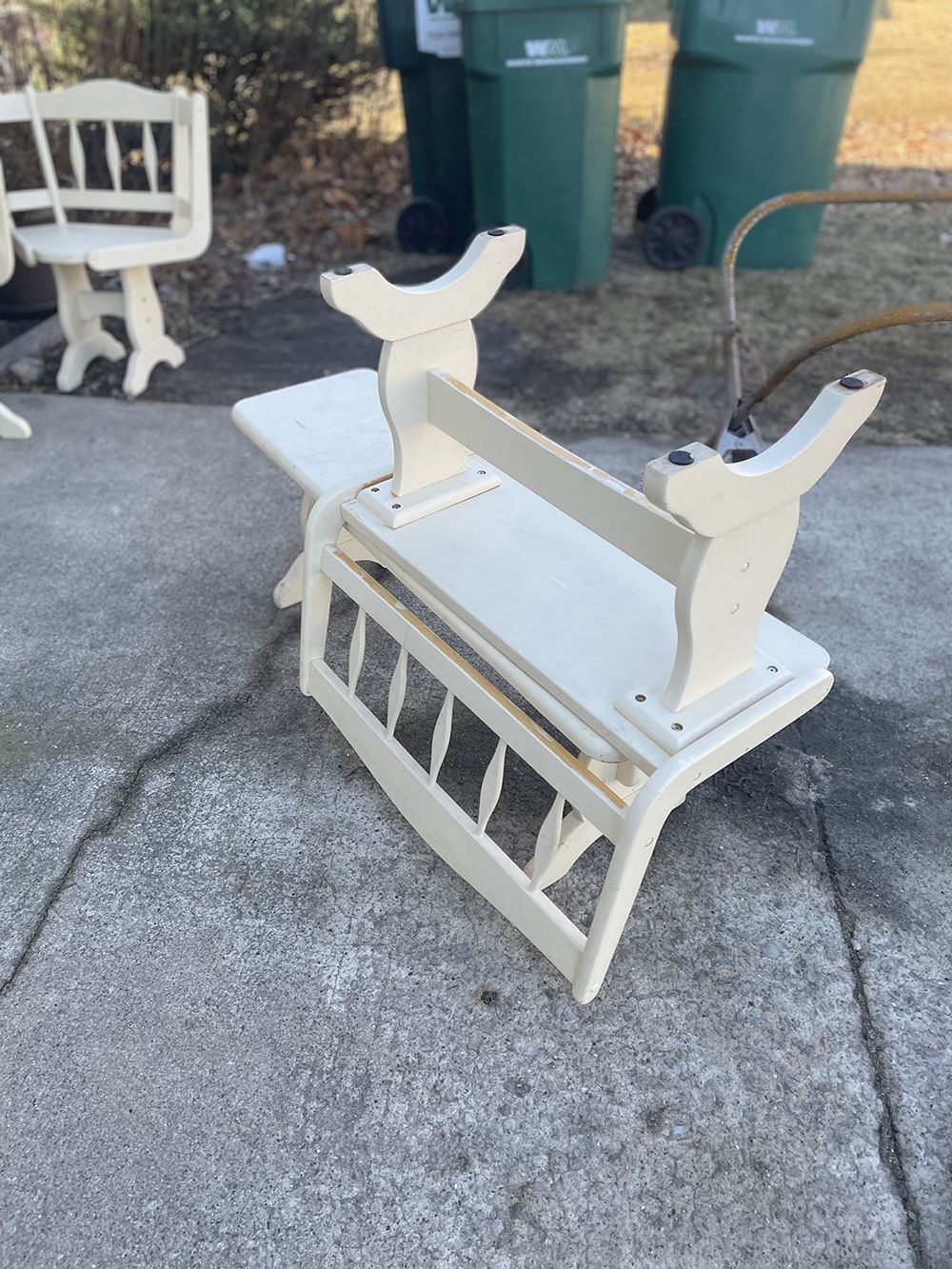 A white bench is sitting on a sidewalk next to a green trash can