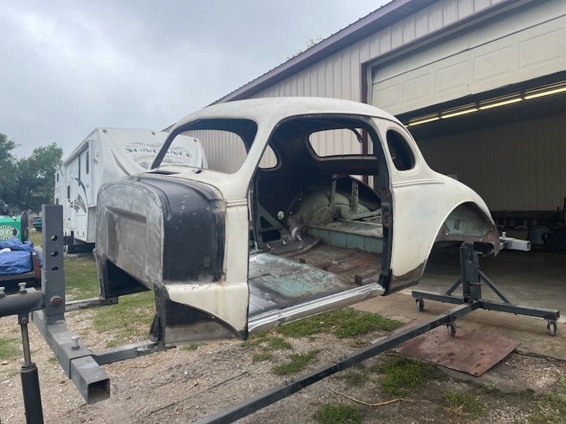 a white muscle car body is sitting on a stand in front of a garage