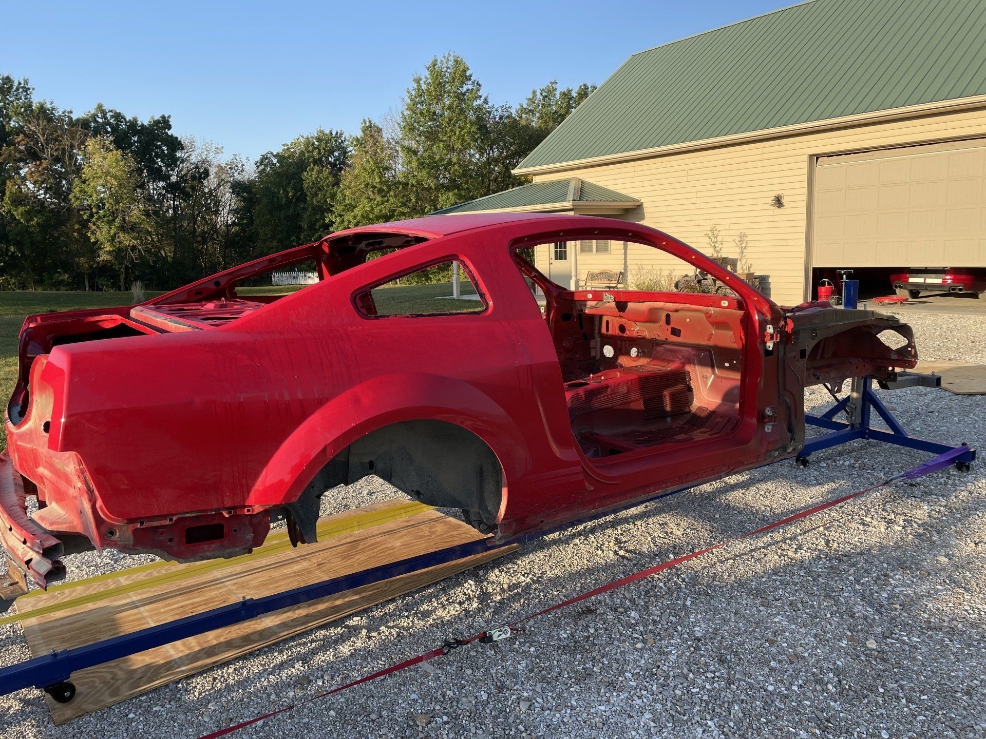 a red muscle car is sitting on top of a gravel road in front of a garage