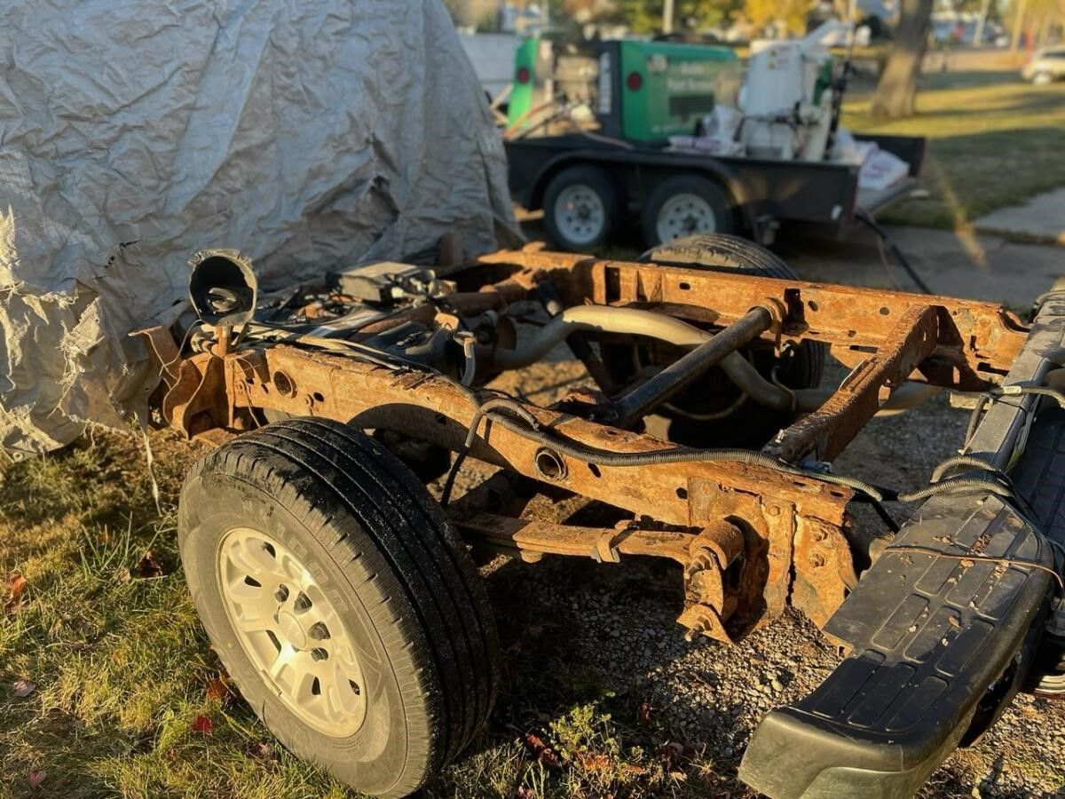 a rusty frame is sitting on the grass next to a trailer
