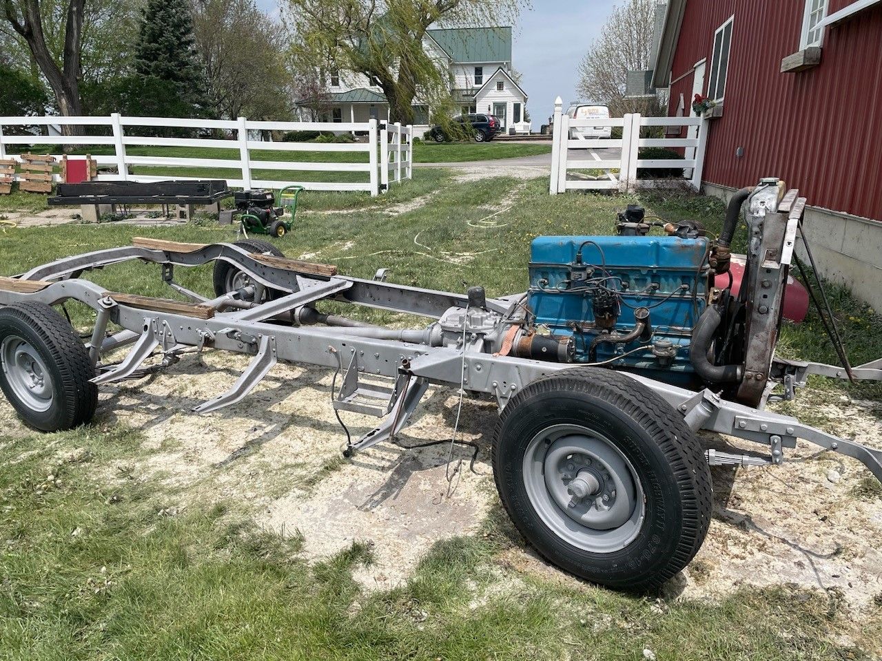 A truck chassis is sitting in the grass next to a barn.