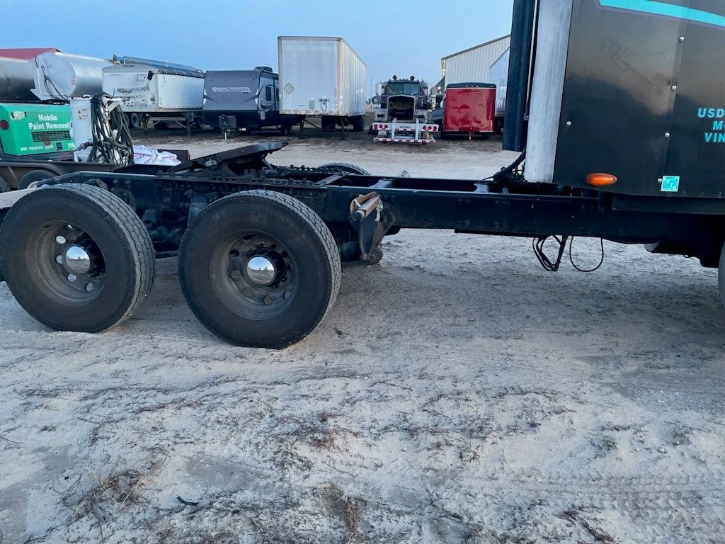 A semi truck with a trailer attached to it is parked in a dirt lot.