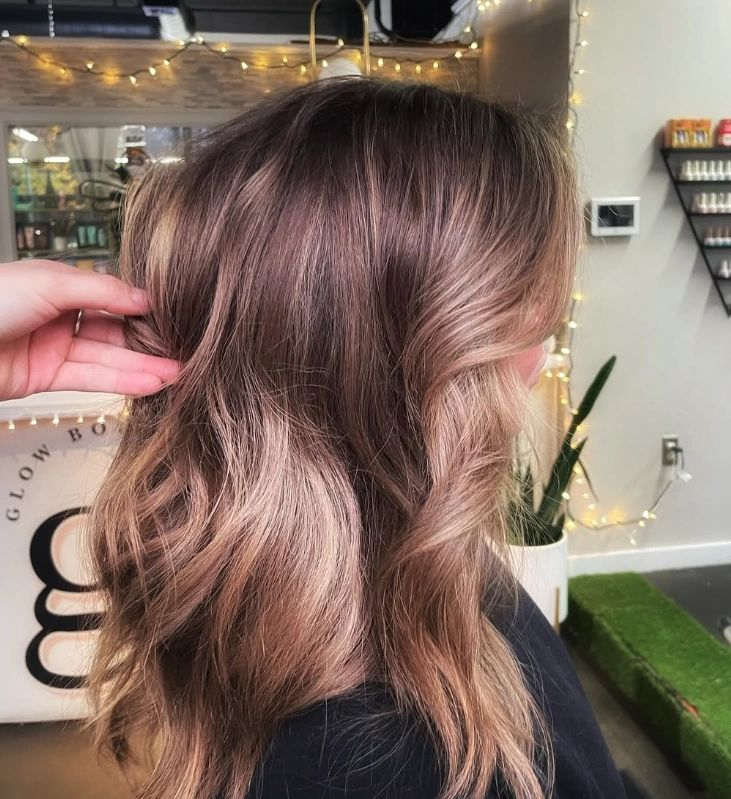 Woman with wavy brown hair, styled with lighter, face-framing highlights. Salon setting.