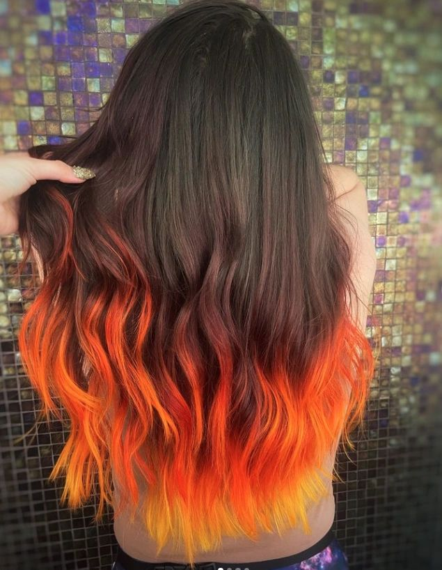 Woman with dark hair transitioning to orange and yellow ombre ends.