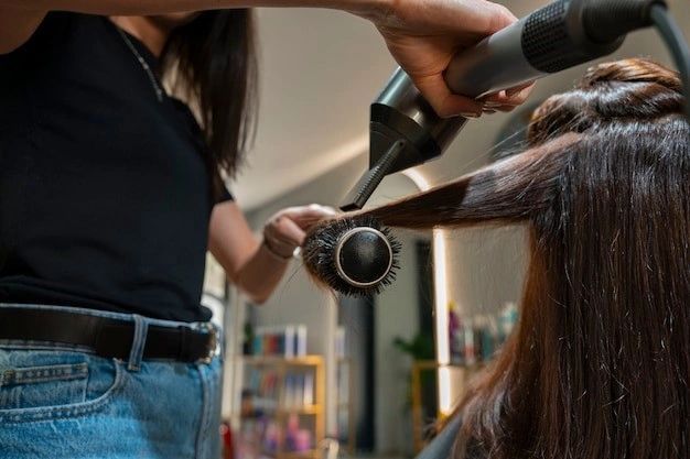 A stylist blow-dries a client's hair with a round brush and hairdryer in a salon.