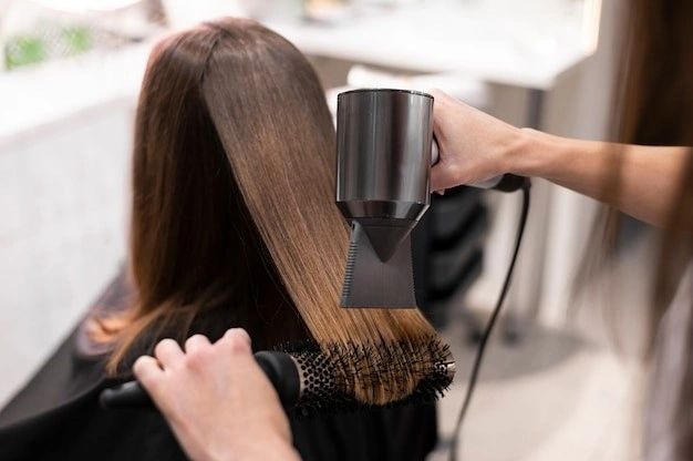 Hairdresser blow-drying a client's brown hair with a brush and hairdryer in a salon.