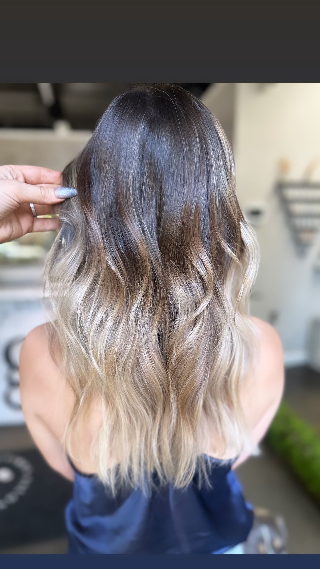 A back view of a person with long, wavy hair transitioning from a dark brown root to light blonde ends.