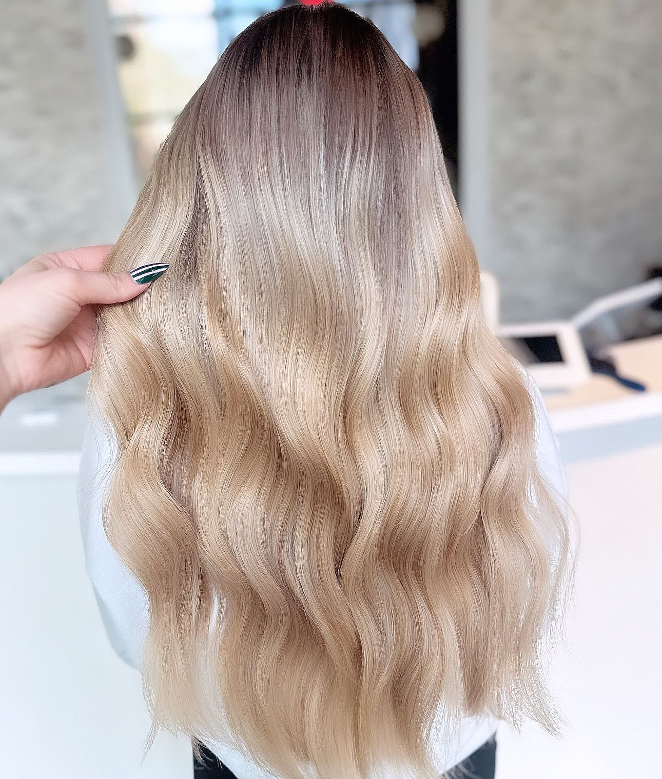Long, wavy hair transitioning from a dark brown root color to a highlighted, multi-tonal light blonde and beige blend.