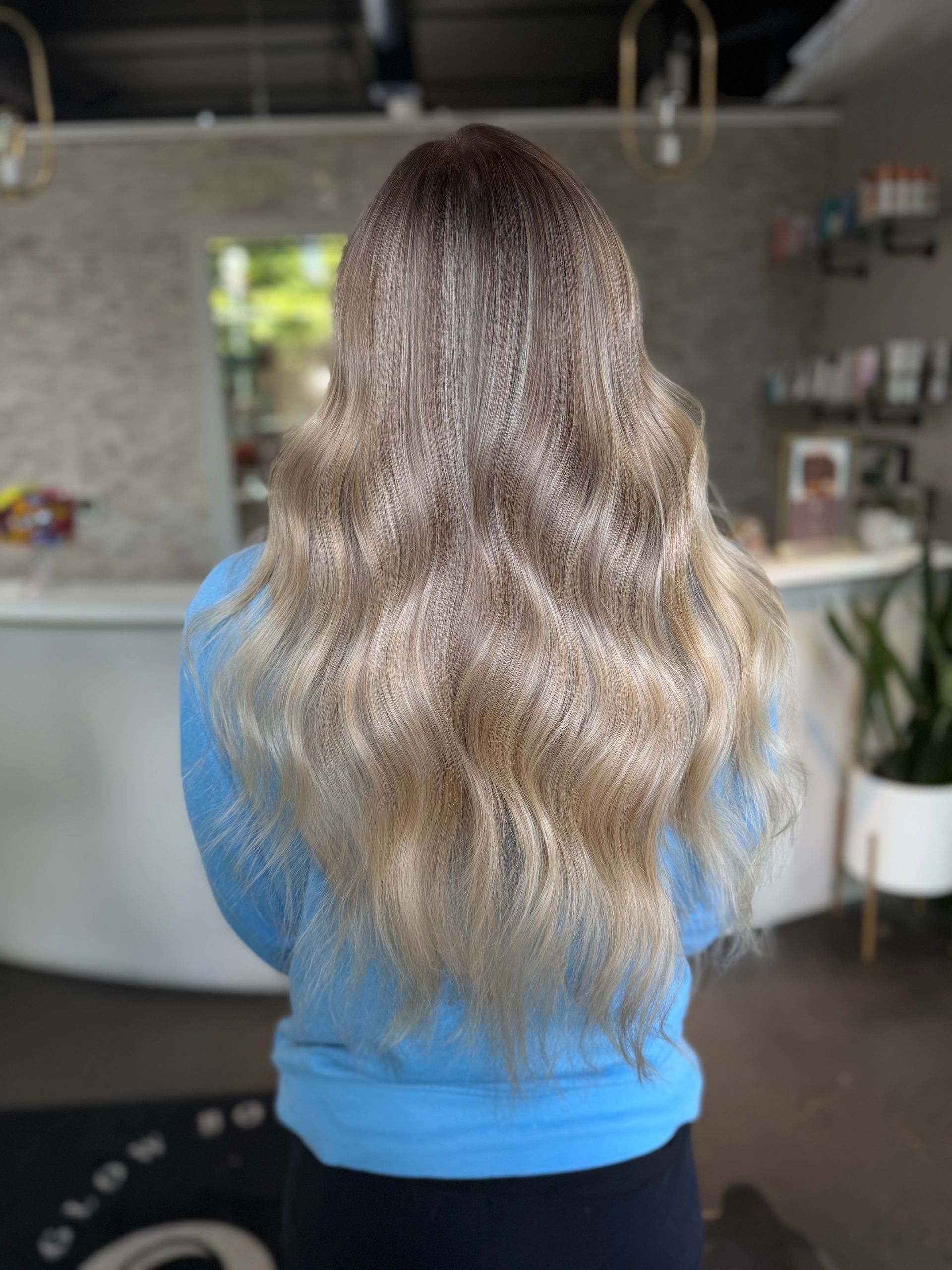 Person seen from behind with long wavy ombré hair, wearing a blue top indoors.