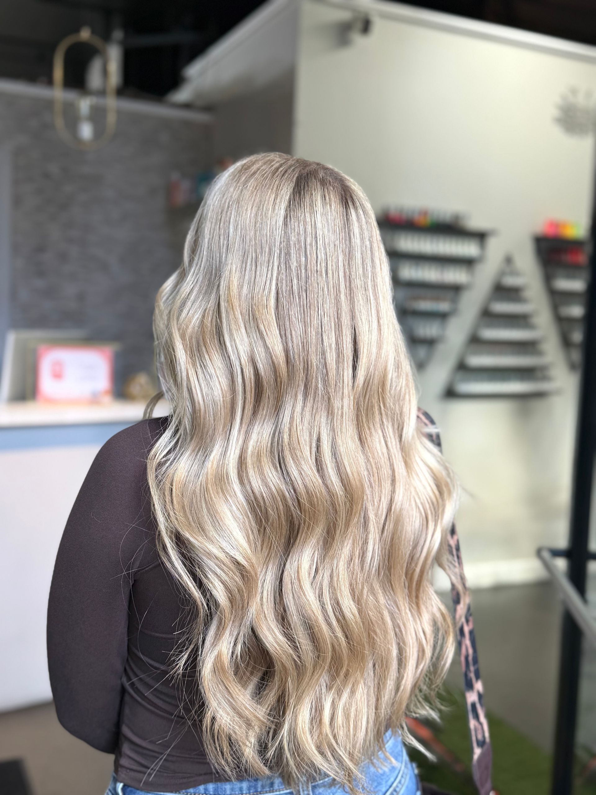 Person with long wavy blonde hair seen from behind in a salon setting.