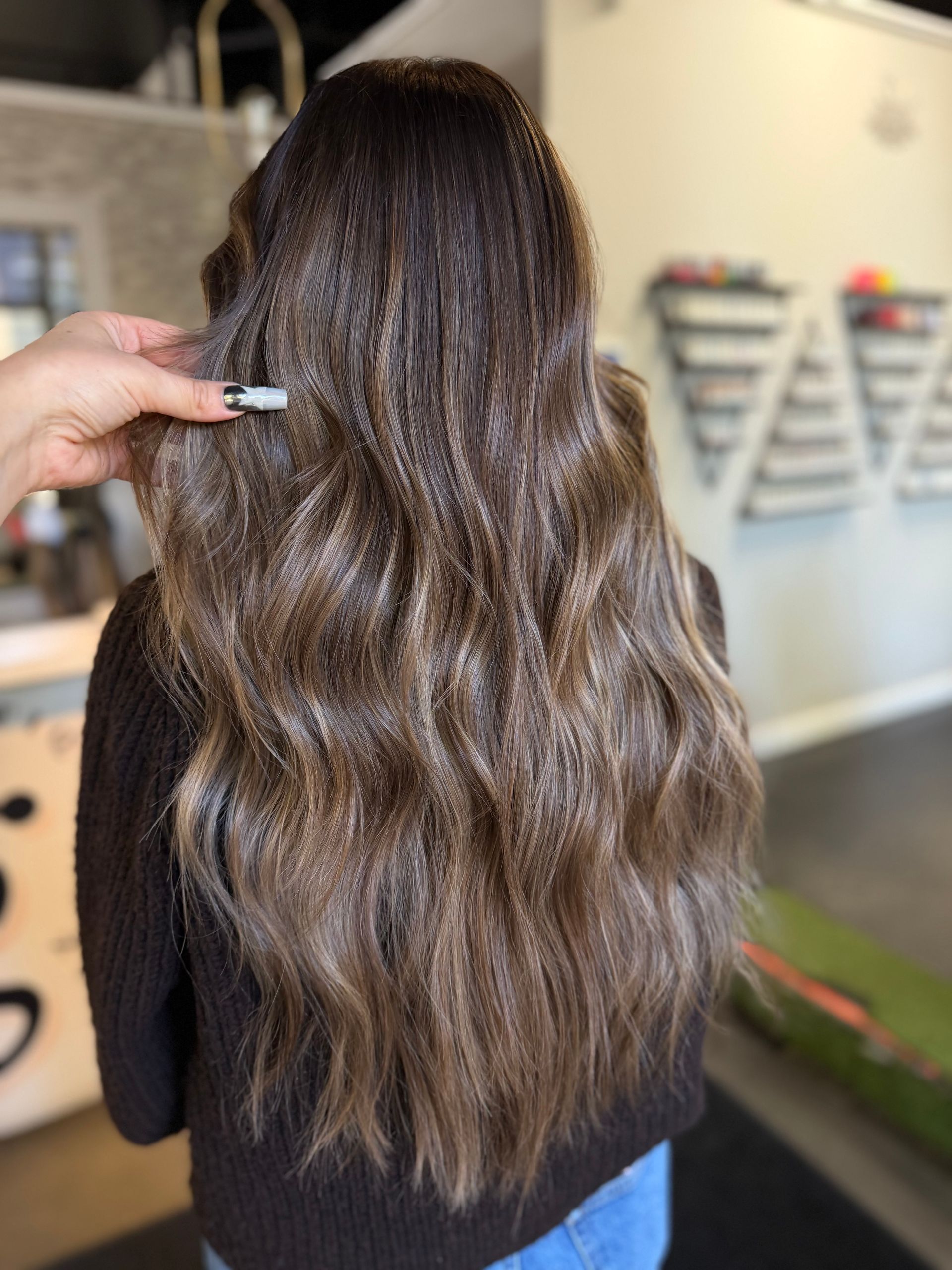 Back view of long wavy brown hair with subtle highlights in a salon setting.