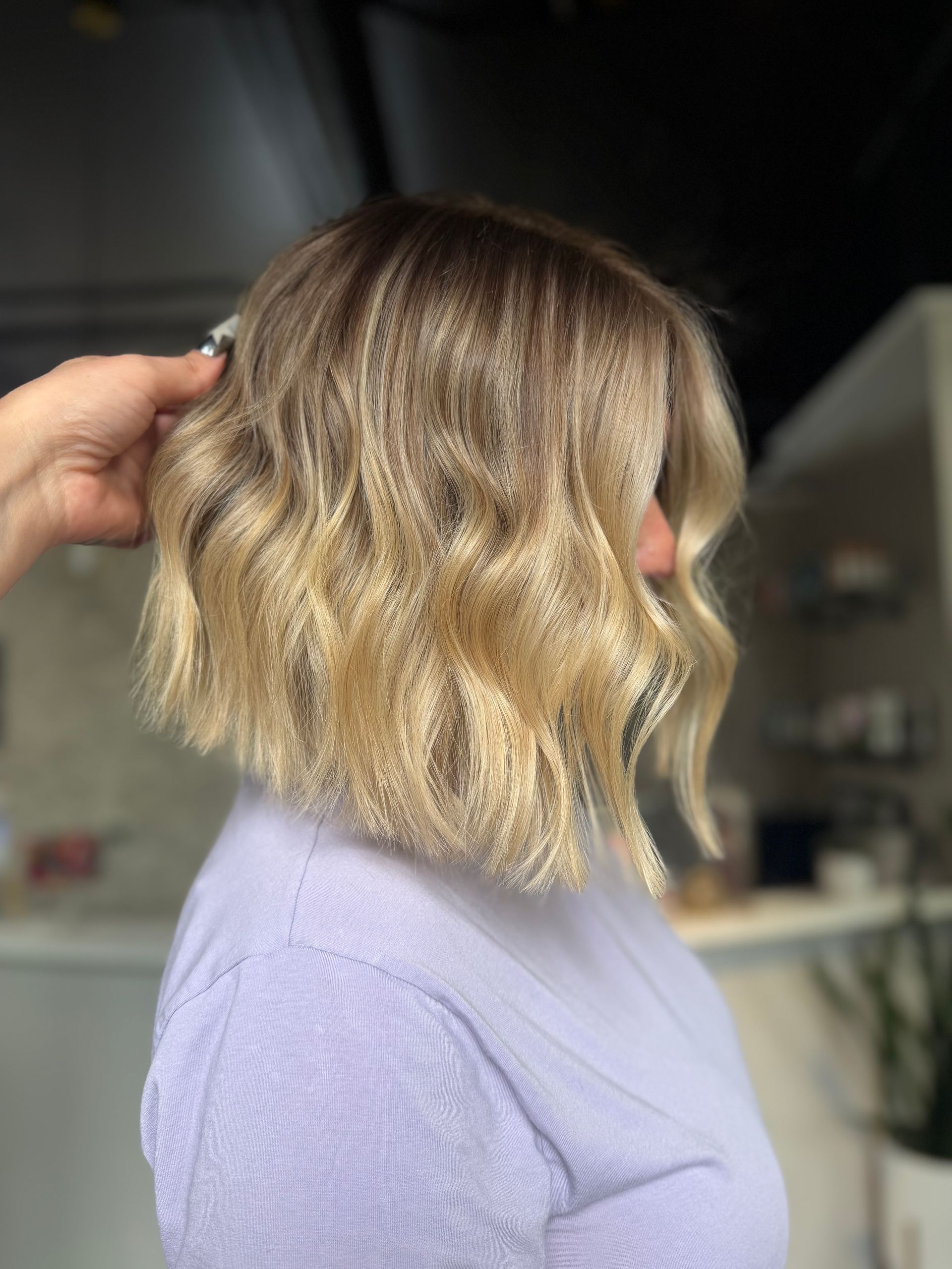 Side view of a wavy blonde bob haircut with dark roots in a salon setting