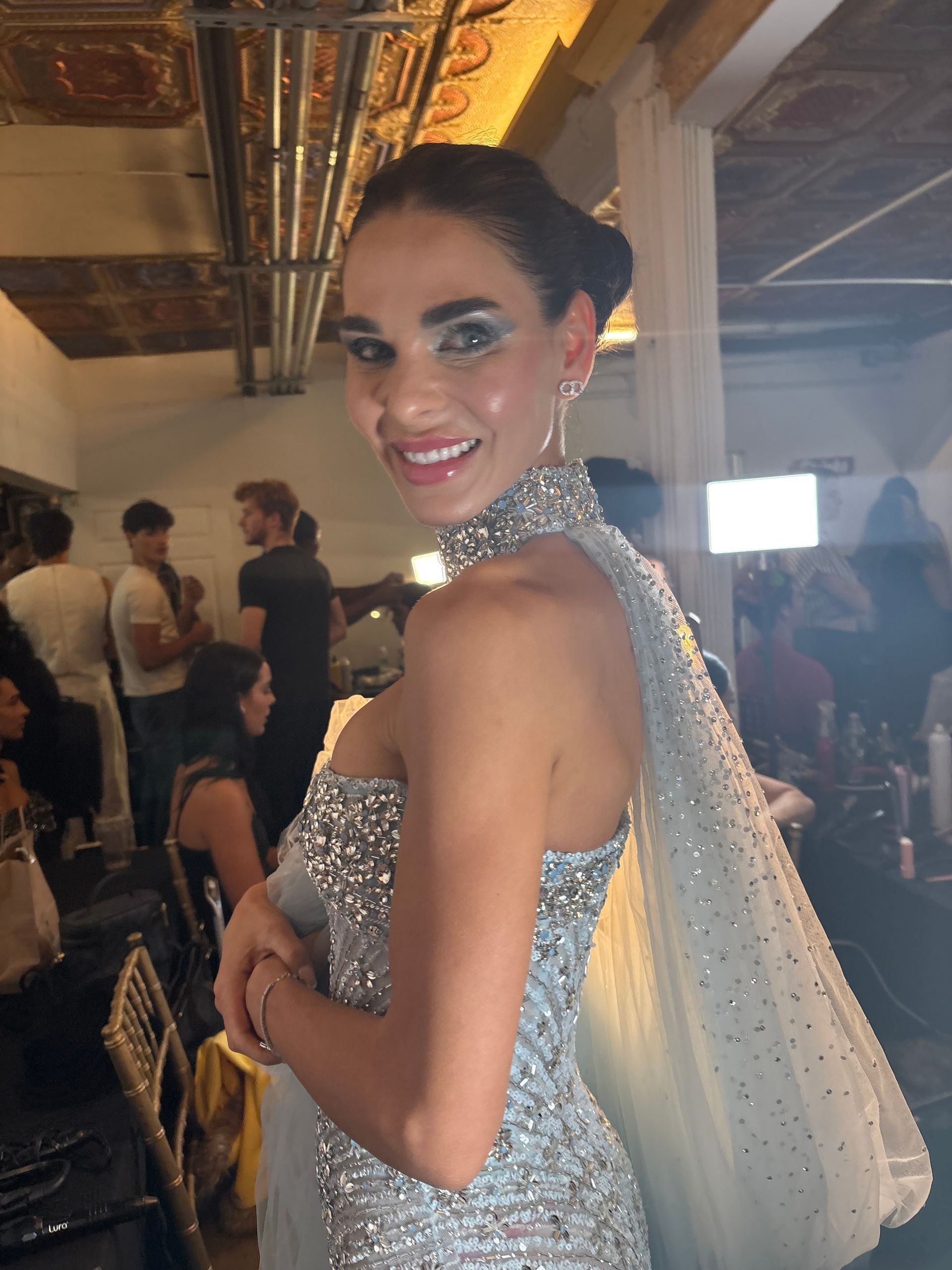 Model in a silver bikini and sheer gold wrap walks the runway before an audience.