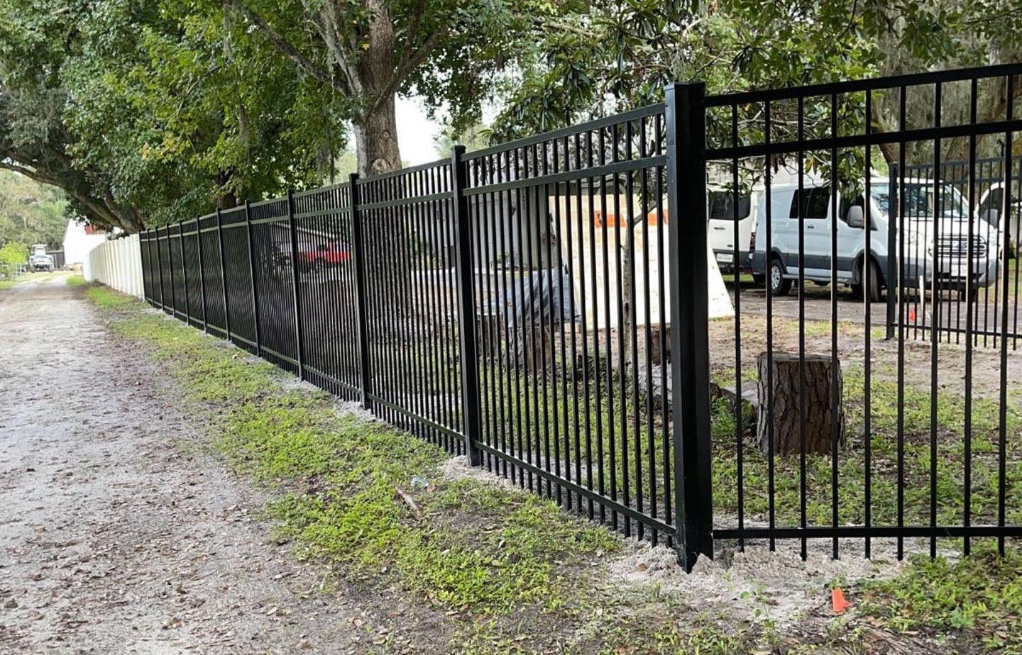 A black metal fence surrounds a dirt road.