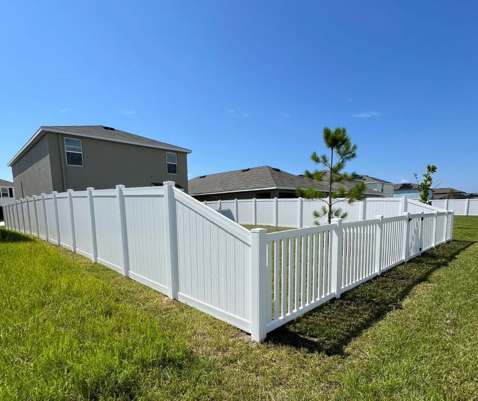 White vinyl fence surrounding a grassy backyard with homes under a clear blue sky.