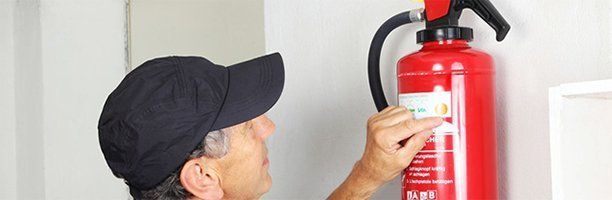 Man in a black cap inspecting a red fire extinguisher attached to a white wall.