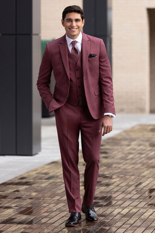 A man in a maroon suit and tie is walking down a sidewalk