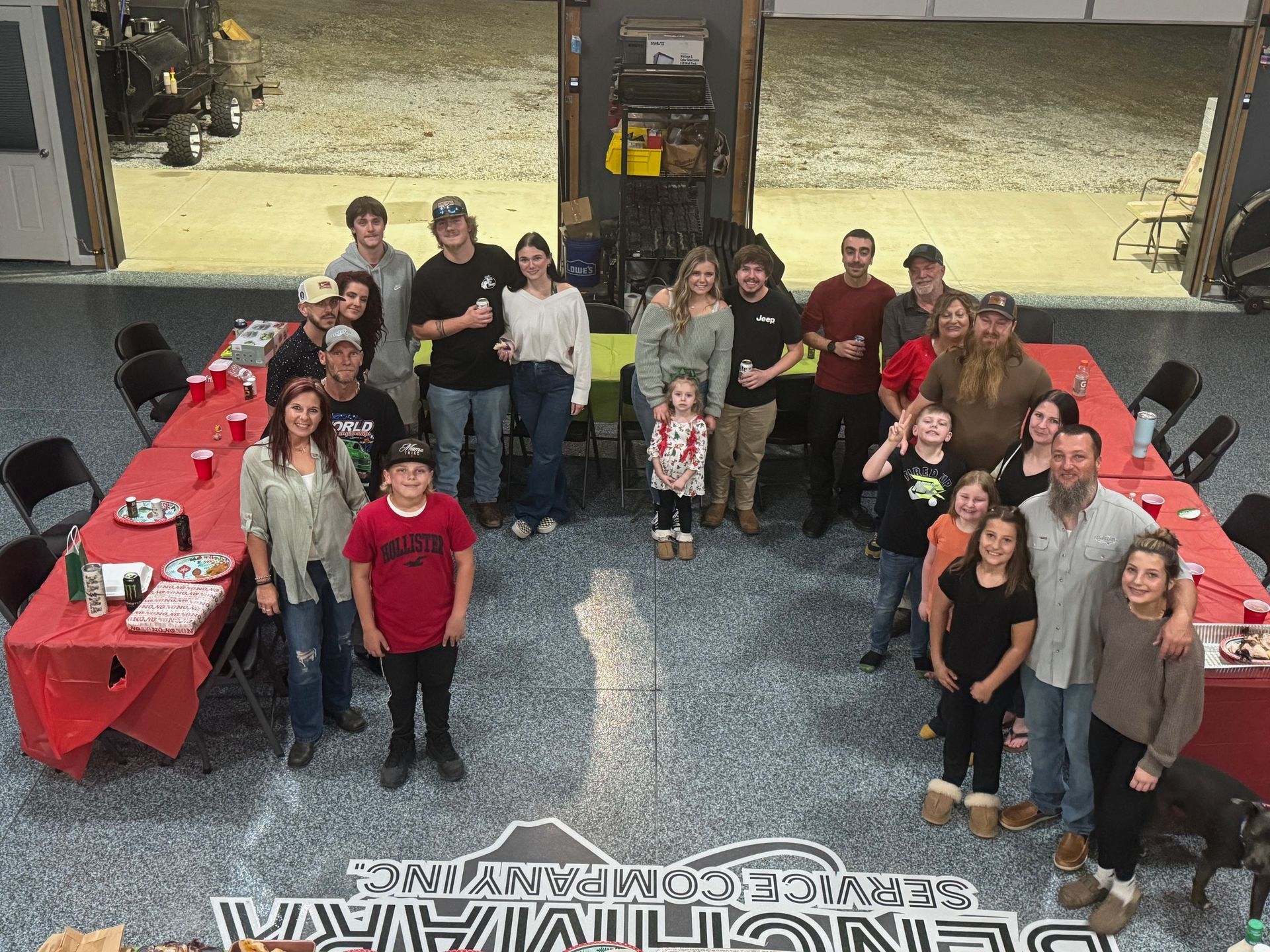 Group of people gathered around a table with food, in a garage-like setting, celebrating.