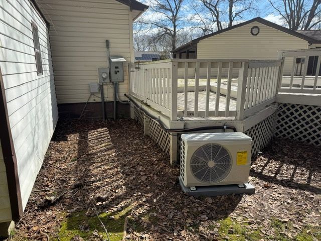 Outdoor air conditioning unit beneath a wooden deck, near beige houses and fallen leaves.
