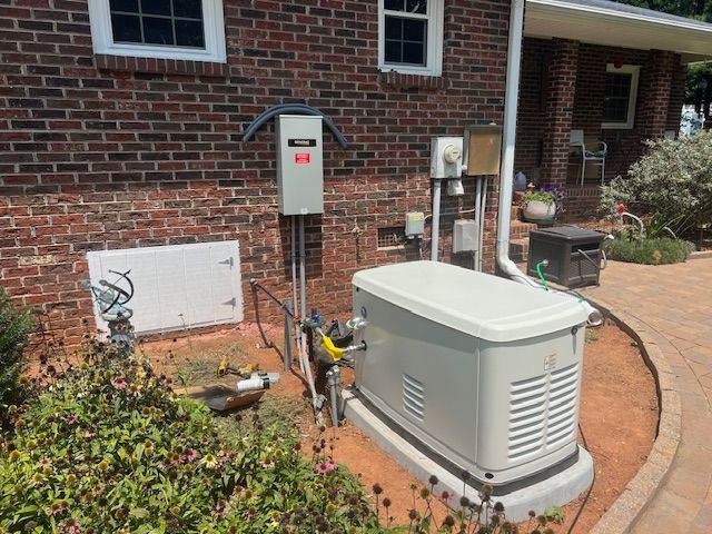 A brick house exterior with a standby generator, electrical boxes, and landscaping.