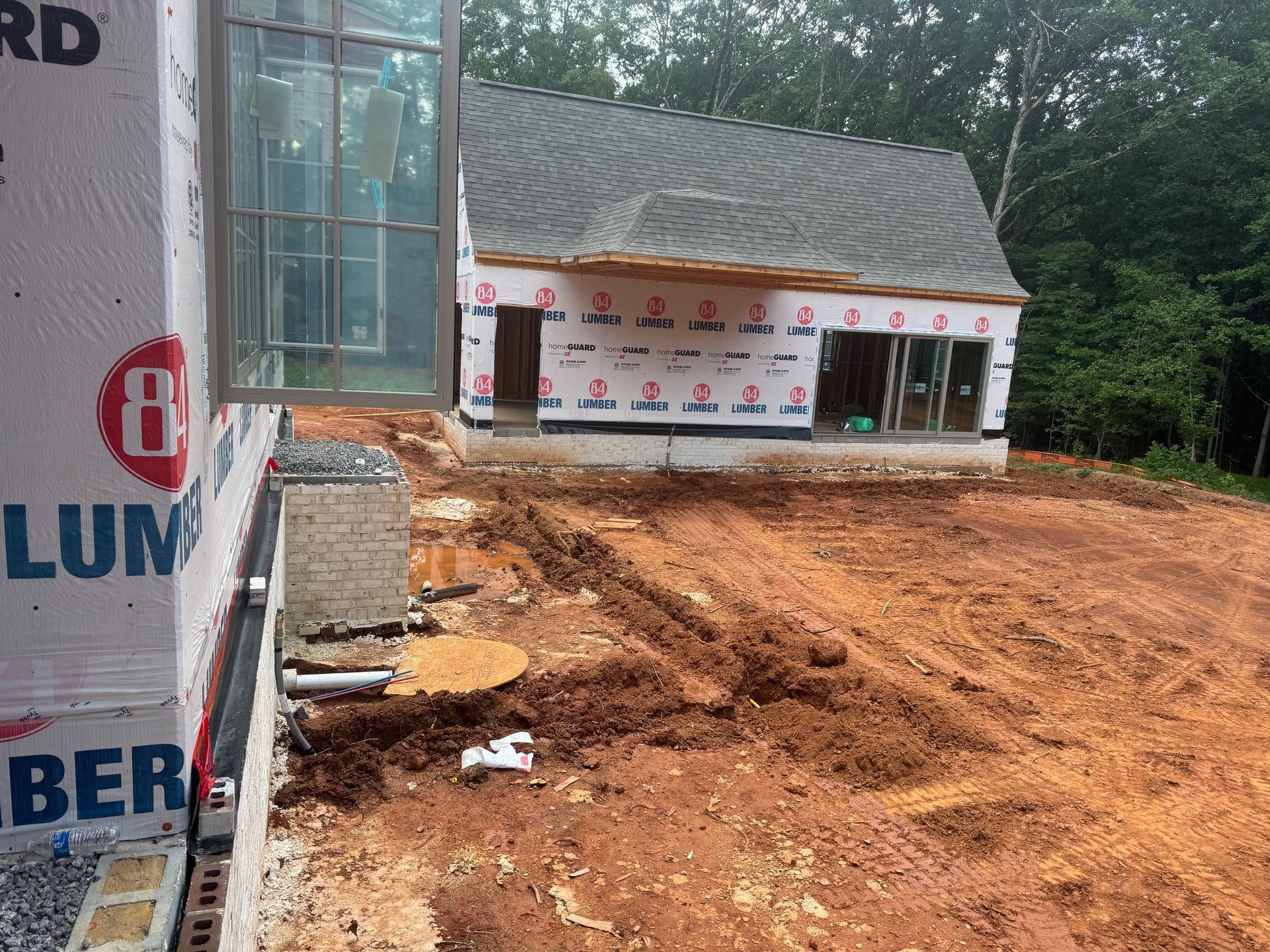 Construction site with a partially built house and red dirt ground.