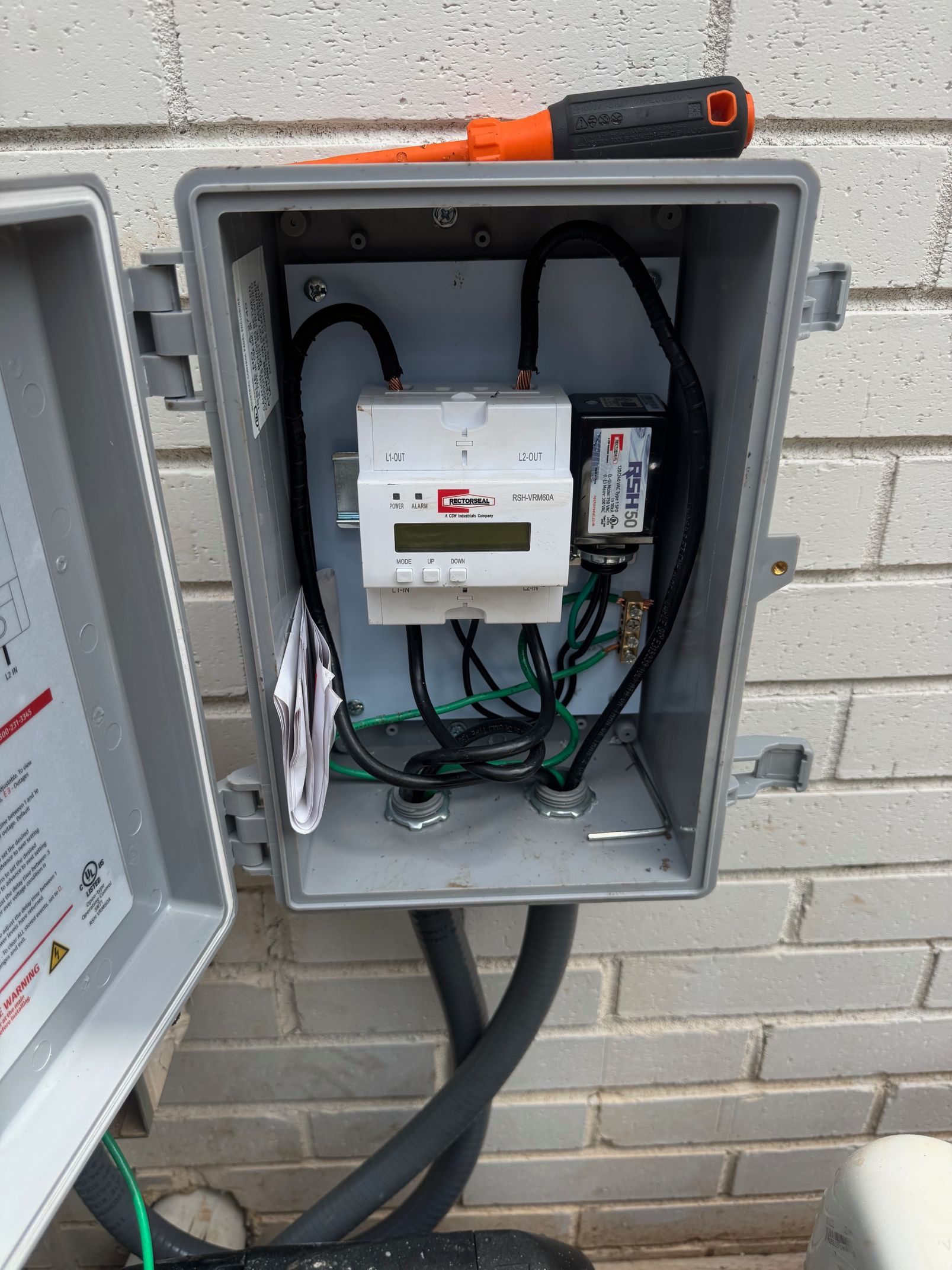 Open electrical box on brick wall, containing a meter, wires, and a screwdriver.