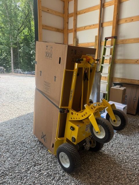 Yellow motorized stair climber carrying a large cardboard box in a garage.