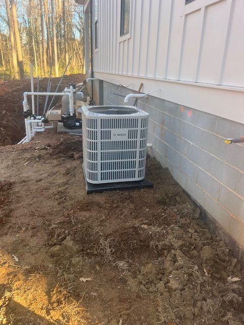 HVAC unit next to a white house with bare earth around it.