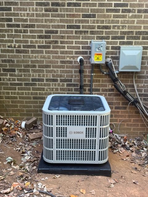 Bosch air conditioning unit on a black pad against a brick wall. Electrical boxes and conduit visible.