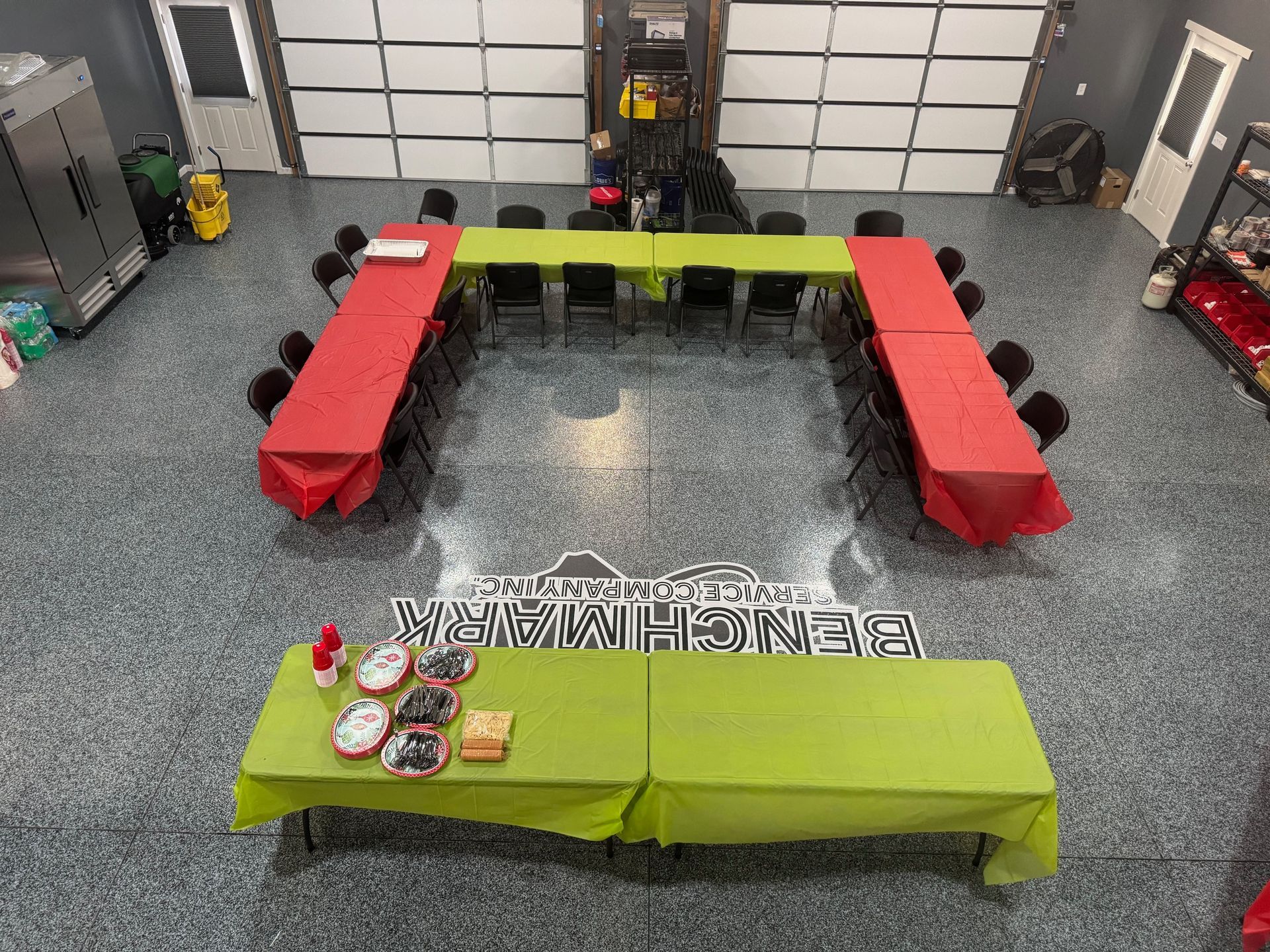 A garage converted to a party space, with tables covered in red and green tablecloths, set for a gathering.