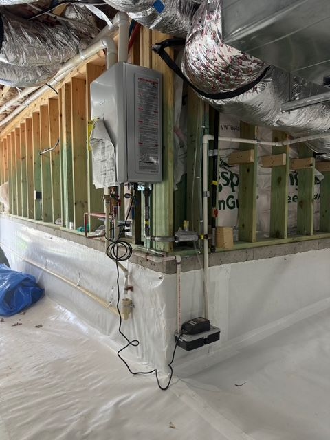 A wall-mounted, tankless water heater in a basement with exposed framing, ductwork, and plastic sheeting.
