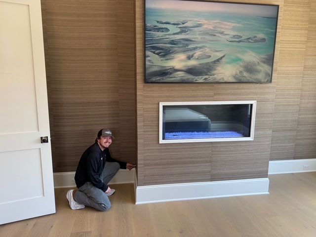 Man kneeling by a white door and baseboard, fireplace and TV mounted on a brown wall.