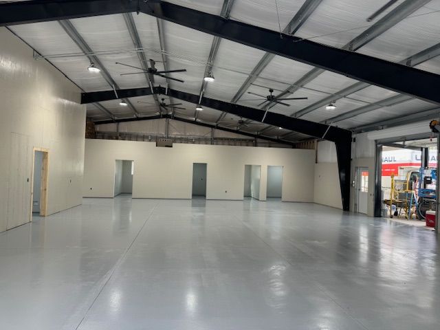 Large, empty commercial interior with a gray floor and tan walls, metal beams, and overhead lights.