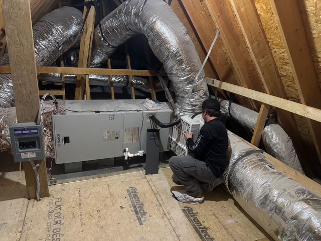 Man inspecting HVAC unit in an attic with ductwork.